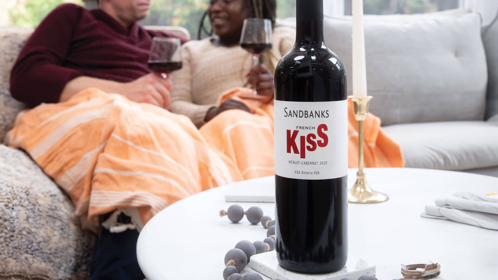 Couple enjoying a glass of Sandbanks French Kiss Merlot-Cabernet cozied up on the sofa. 