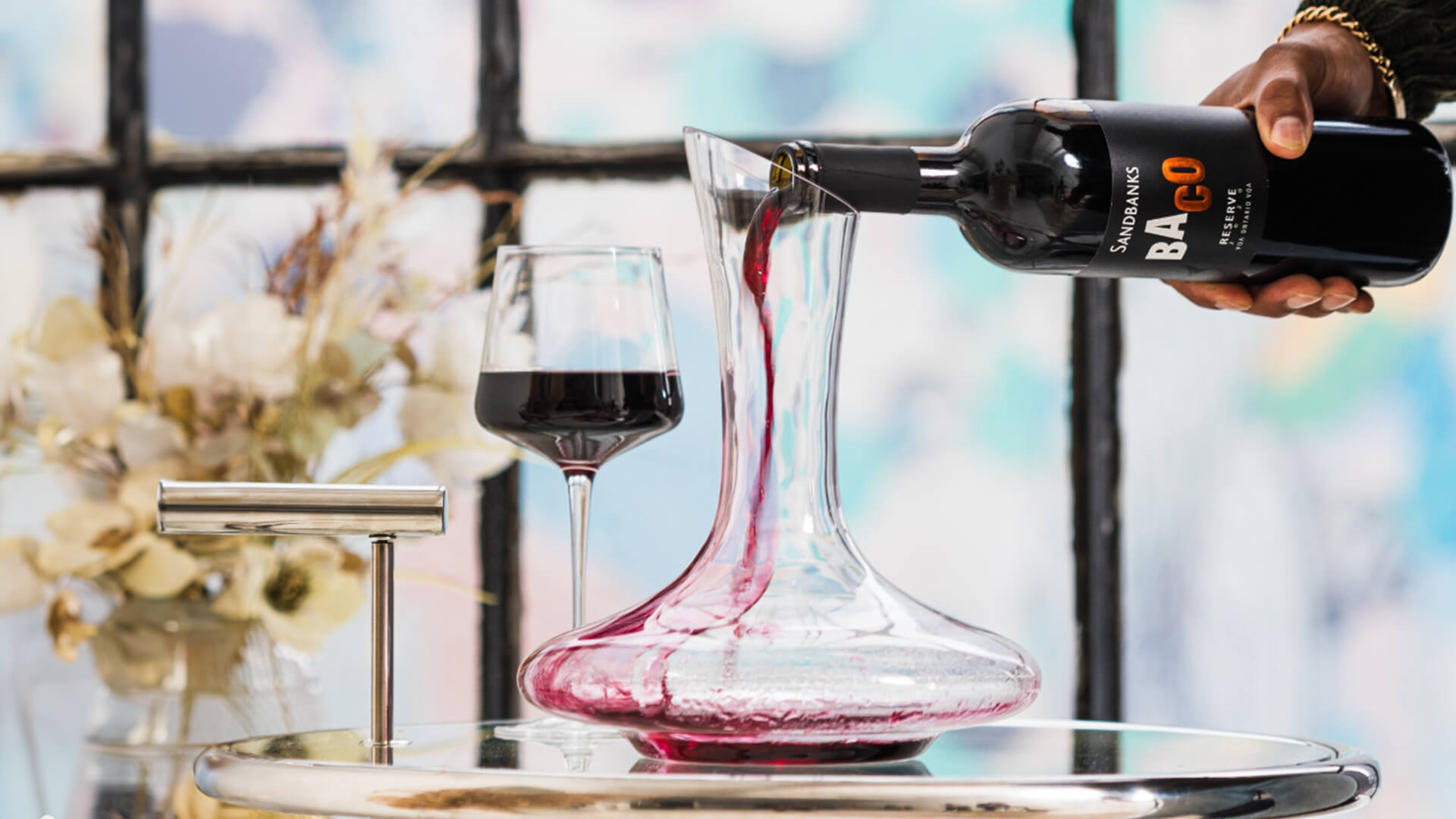 A bottle of Sandbanks Baco Noir being poured into a decanter.